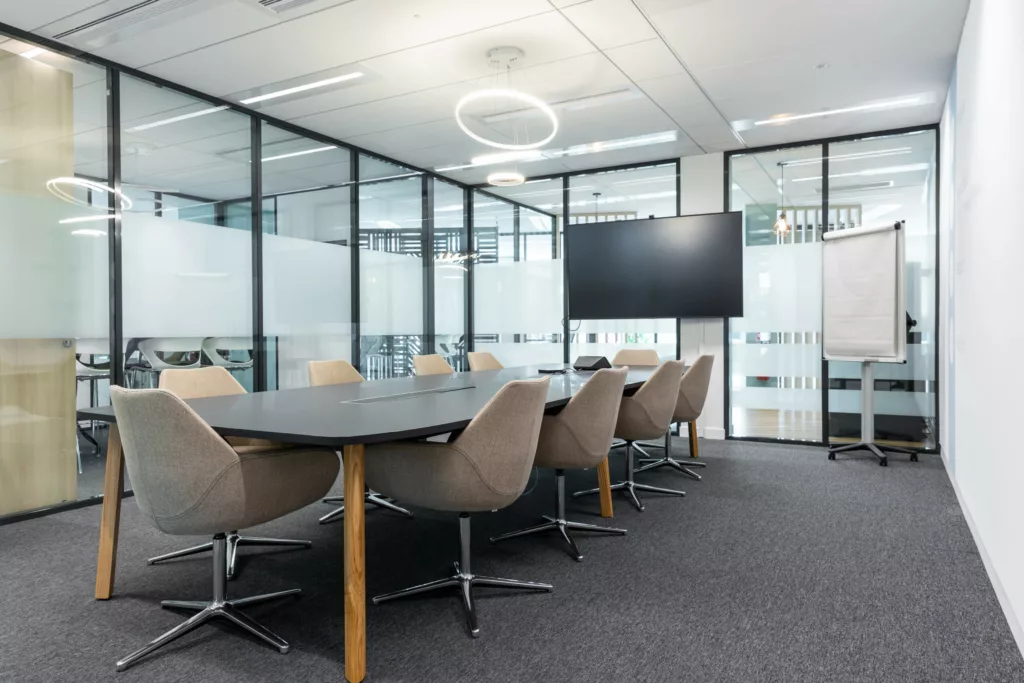 Grande salle de réunion équipée d'une table de conseil et de fauteuils ergonomiques sous cloisons vitrées.