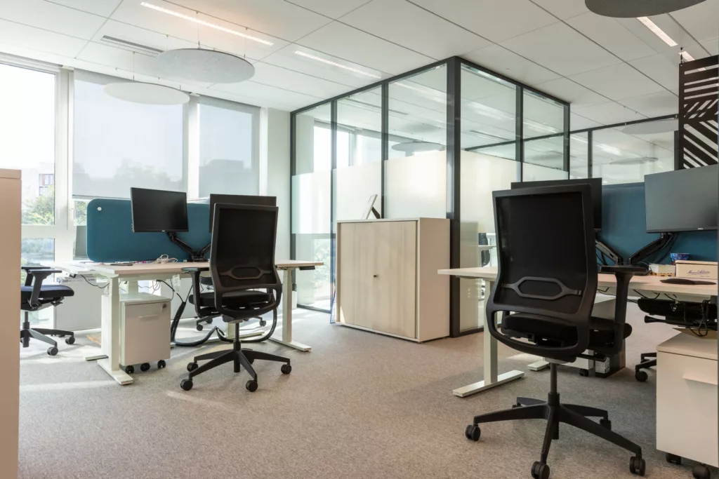 Postes de travail ergonomiques avec bureaux assis-debout et séparateurs acoustiques en open space.