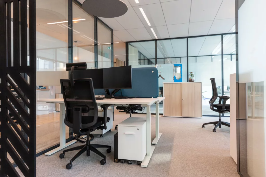 Bureau individuel aménagé avec double écran et écran de séparation acoustique bleu.