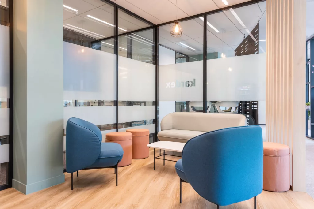 Espace de réunion informelle équipé de fauteuils bleus, d'un canapé et de poufs colorés.