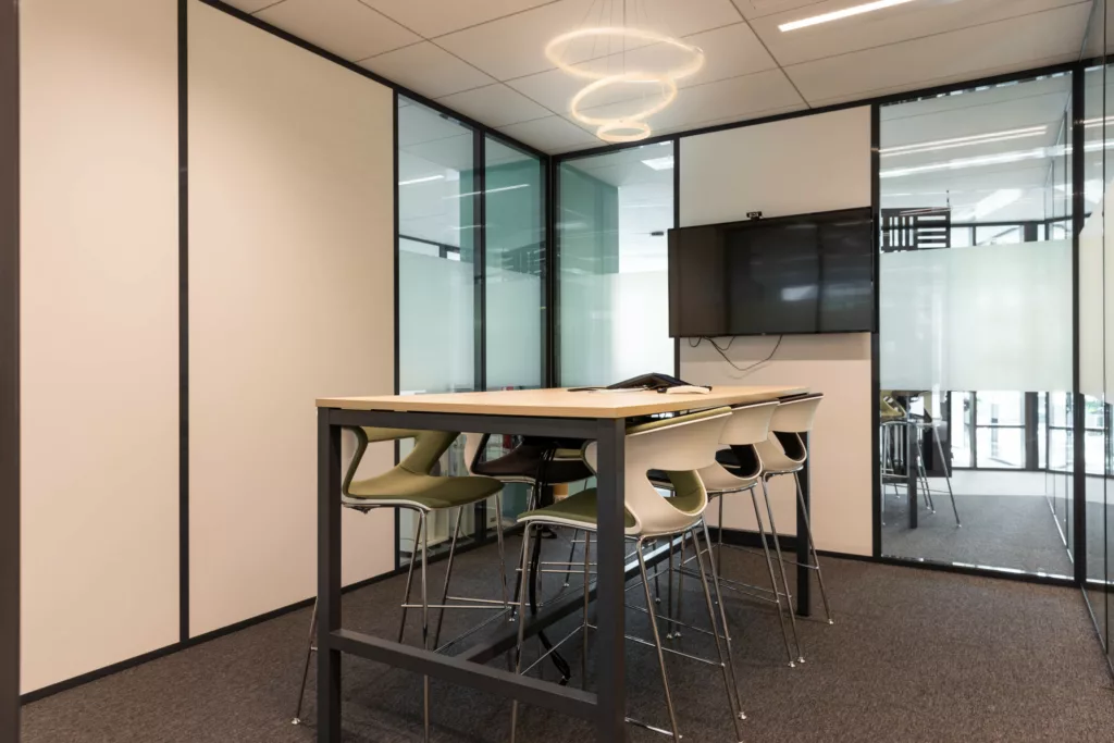 Salle de réunion agile avec table haute, tabourets design et écran de présentation.