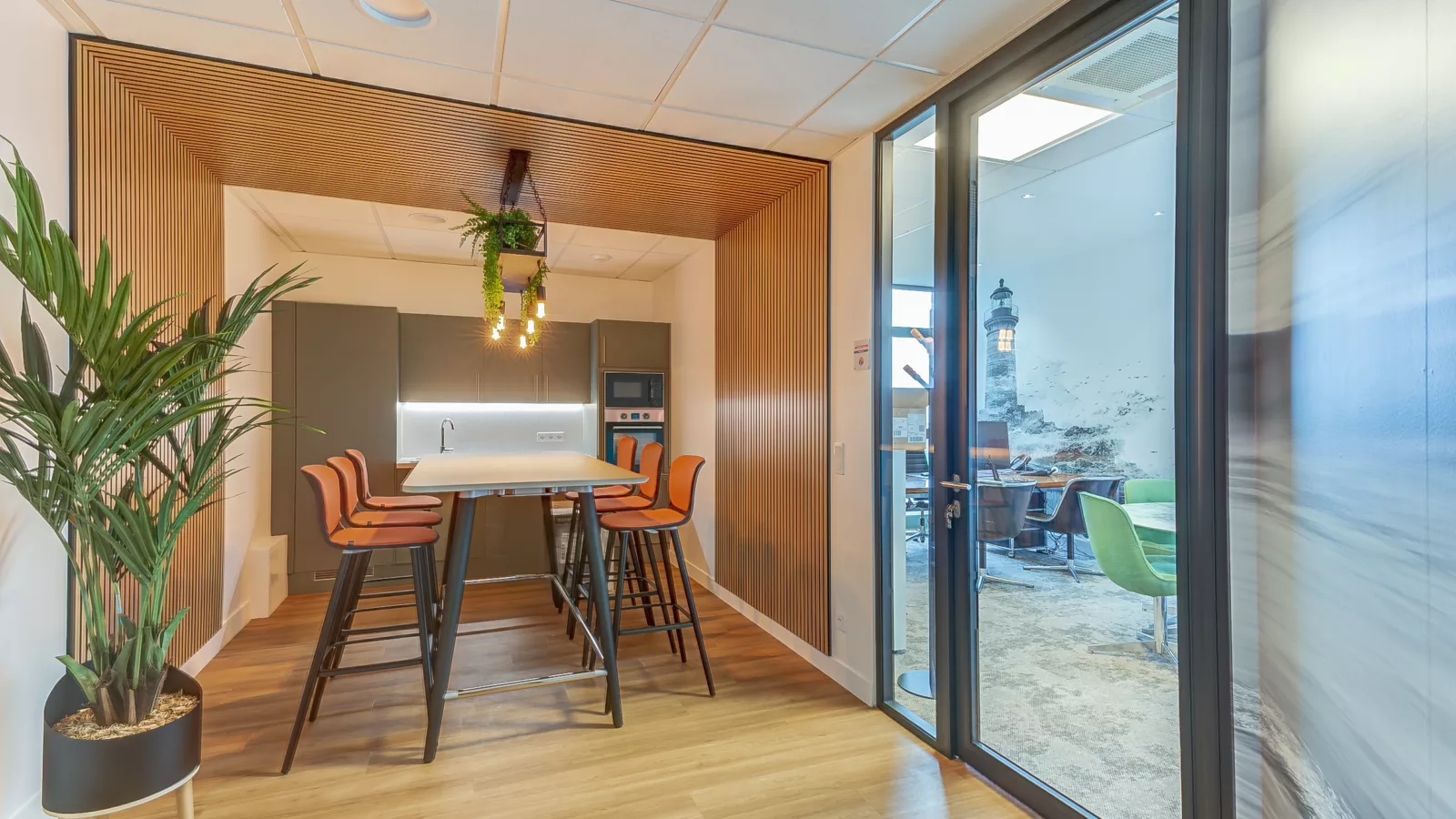 Aménagement de la kitchenette et de l'espace repas dans les bureaux de S3R à Noisy-le-Roi (78). Panneaux acoustiques en bois (tasseaux) et mobilier haut.
