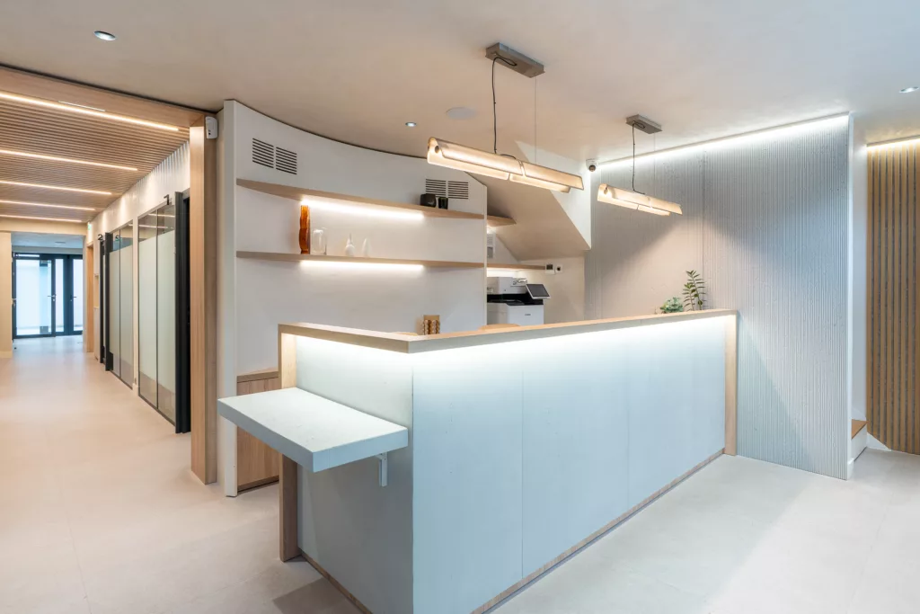 Banque d'accueil sur mesure pour cabinet dentaire et de chirurgie à Ivry-sur-Seine (94). Comptoir moderne avec éclairage LED intégré et étagères décoratives en bois