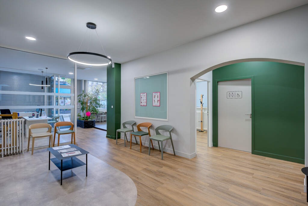 Rénovation complète d'une salle d'attente et WC PMR à Paris Nation par AMSO. Sol PVC en courbe délimitant l'espace et grand mur décoratif pour ambiance chaleureuse