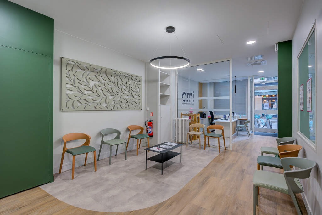 Salle d'attente et zone d'accueil du centre de santé AMI. Rénovation AMSO montrant la pose de sols PVC en courbe pour délimiter les espaces, un grand panneau acoustique décoratif et la banque d'accueil au fond