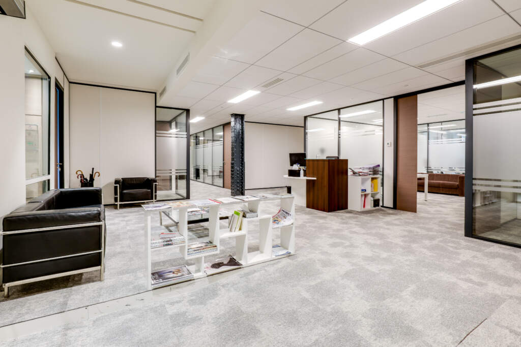 Espace d'accueil d'entreprise moderne avec canapés en cuir noir, meuble bibliothèque design et cloisons vitrées, réalisé par AMSO.