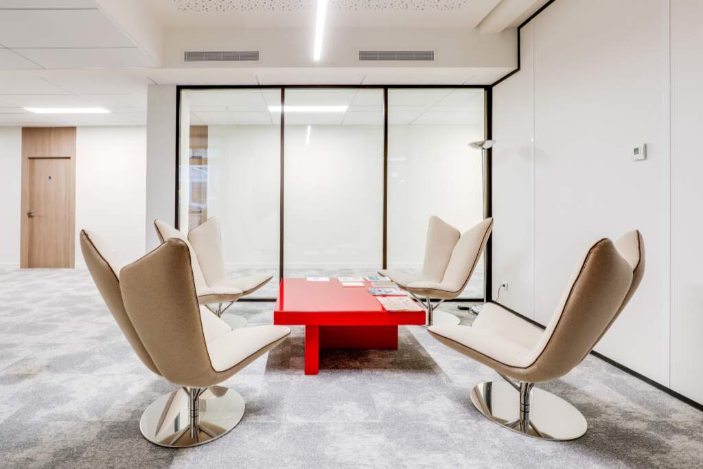 Coin détente d'entreprise avec fauteuils design beiges et table basse rouge vif, un agencement d'espaces pensé par AMSO.