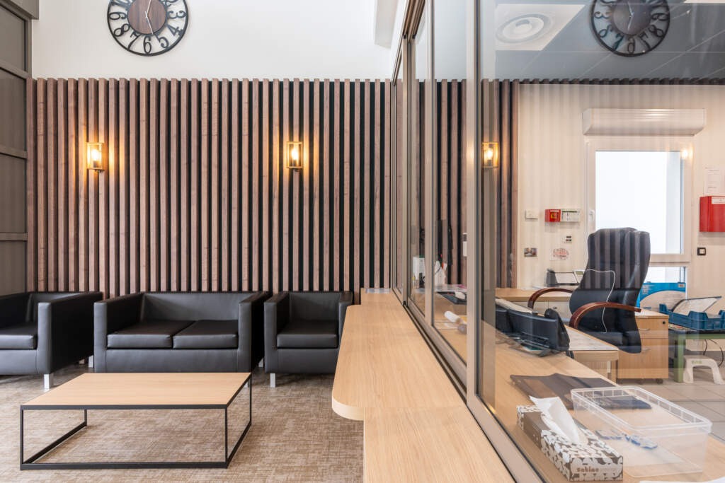 Espace d'attente de bureau moderne et accessible aux fauteuils roulants, avec canapés en cuir et mur acoustique en bois.