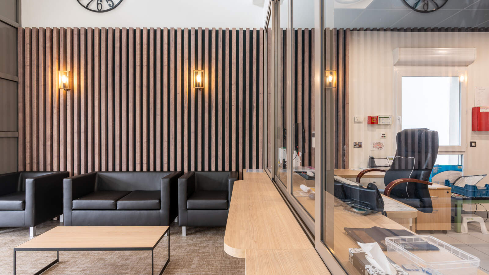Espace d'attente de bureau moderne et accessible aux fauteuils roulants, avec canapés en cuir et mur acoustique en bois.
