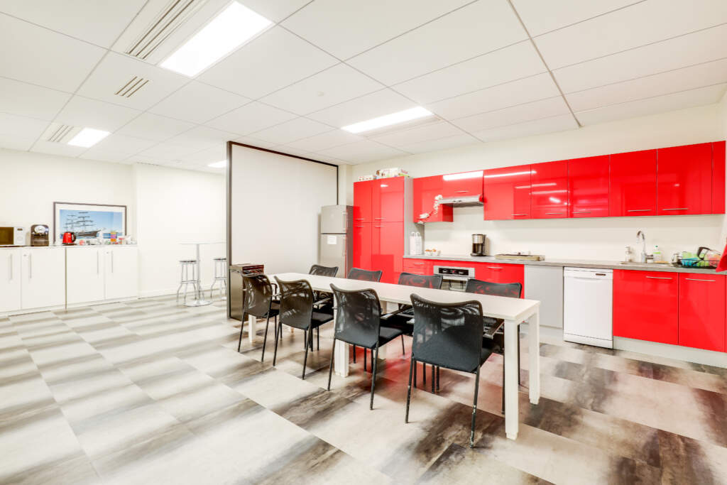 Grande cuisine d'entreprise moderne avec meubles rouges laqués, grand plan de travail et espace repas, aménagée par AMSO.