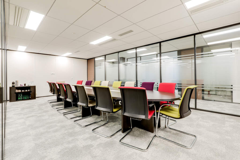 rande salle de réunion moderne avec table ovale, fauteuils de couleur et cloisons vitrées, aménagée par le contractant AMSO.