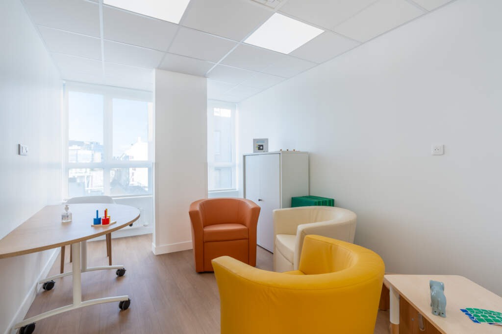 Bureau de consultation avec fauteuils de couleur (jaune, orange), table ronde et placard de rangement sur mesure.