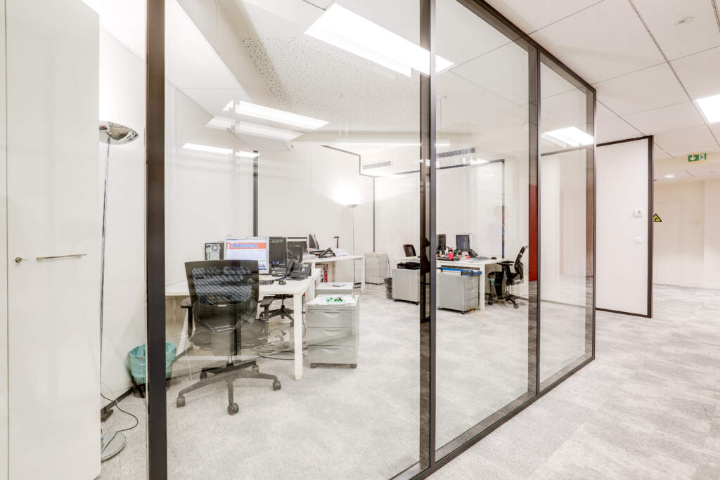 Espace de travail isolé par des cloisons vitrées façon bulle de confidentialité au sein d'un grand plateau de bureaux par AMSO.