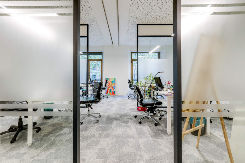 Vue à travers une cloison vitrée avec vitrophanie sur un espace de travail ouvert et créatif, aménagement signé AMSO.