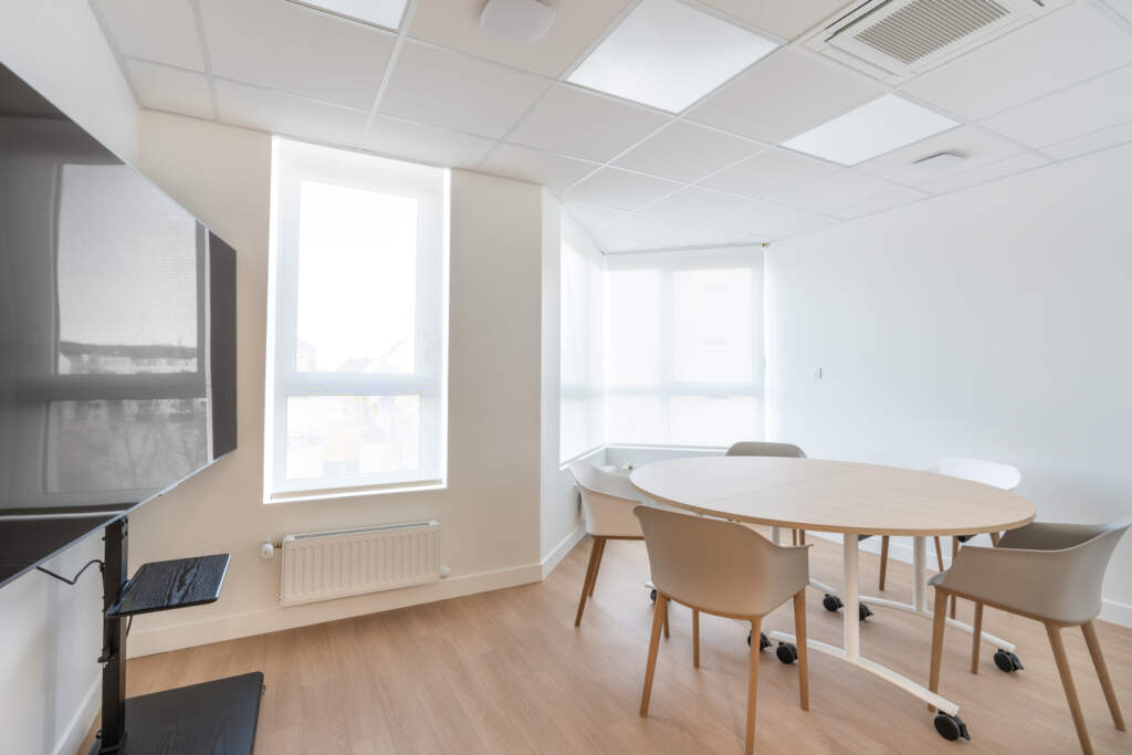 Salle de réunion avec table ronde, écran TV et stores intérieurs AMSO.