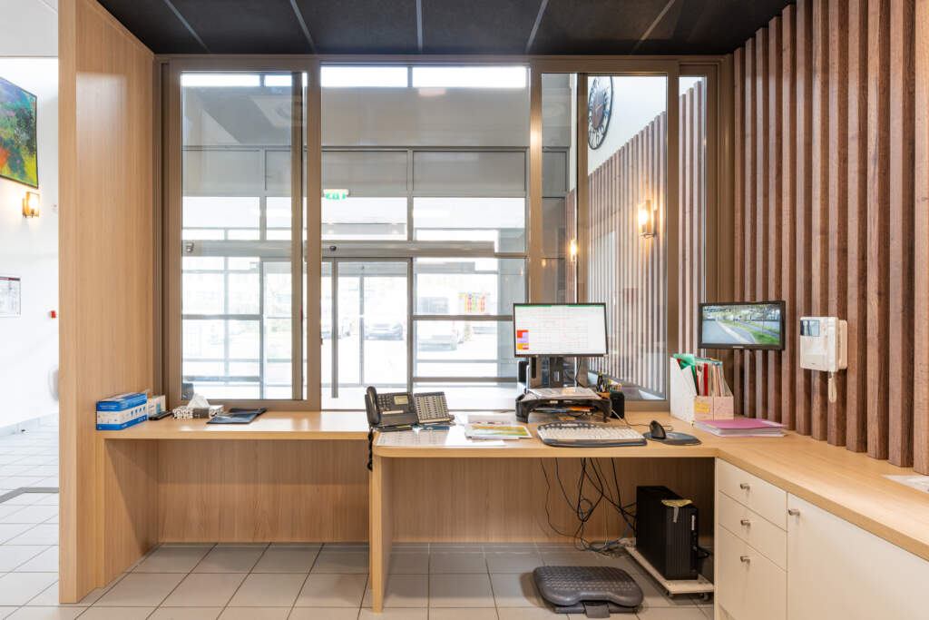 Poste de travail d'accueil en bois avec comptoir surbaissé et espace dégagé, réalisé lors de travaux d'accessibilité.