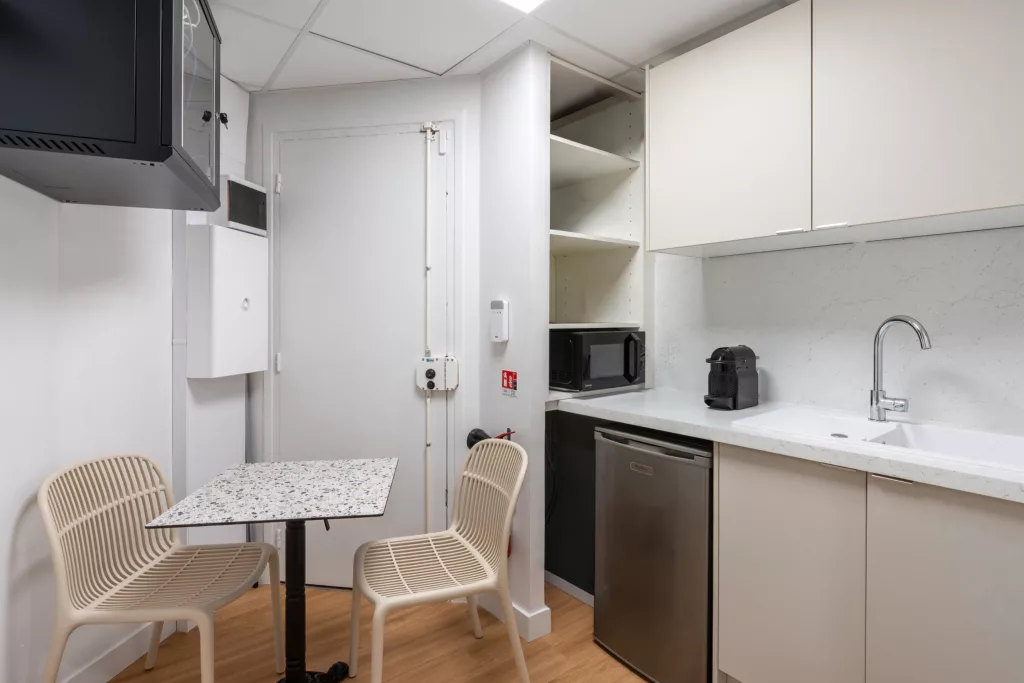 Petite salle de repos pour le personnel soignant avec kitchenette intégrée, micro-ondes, réfrigérateur et table bistrot.