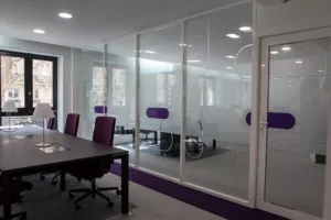 Salle de réunion moderne avec table sombre, chaises violettes et cloisons vitrées sur mesure.