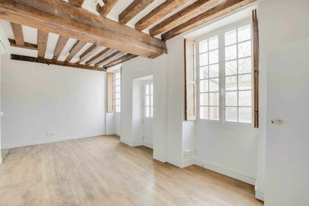 Pièce lumineuse entièrement rénovée avec poutres en bois apparentes au plafond et murs blancs.
