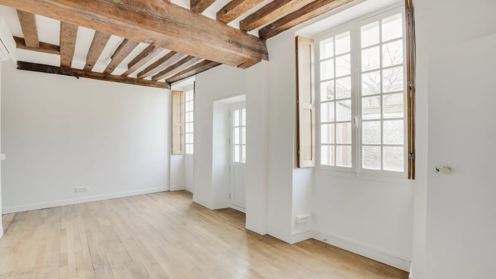 Pièce lumineuse entièrement rénovée avec poutres en bois apparentes au plafond et murs blancs.