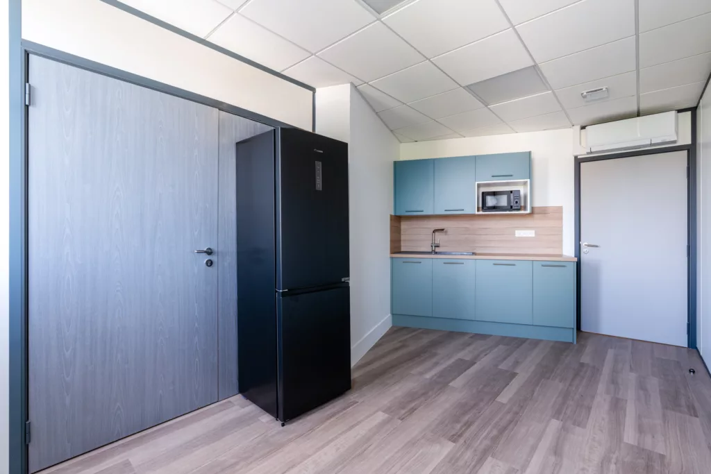 Cuisine de bureau aménagée avec meuble sur mesure bleu canard, crédence bois et réfrigérateur.