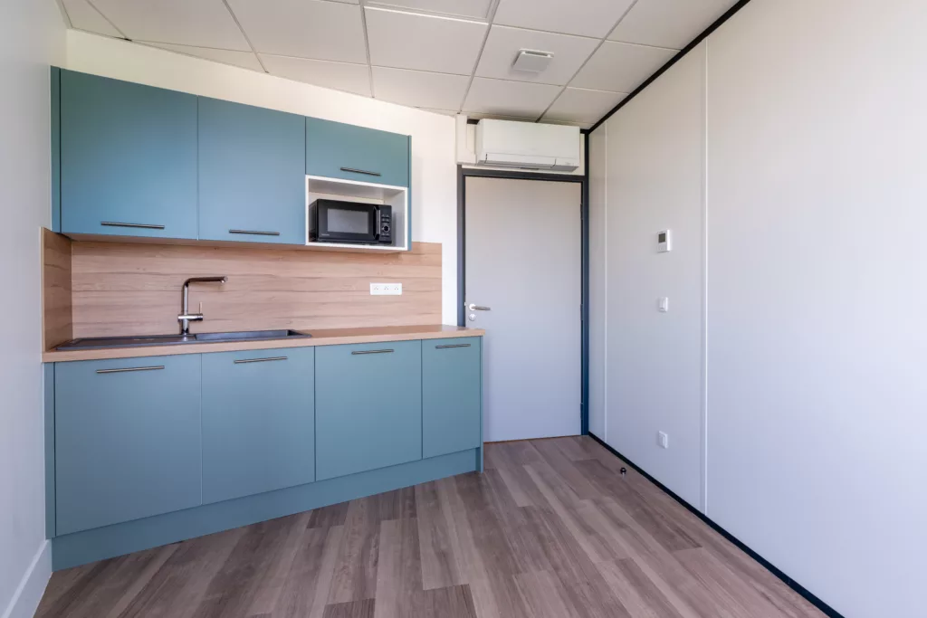 Cuisine équipée compacte pour locaux professionnels avec meubles haut/bas et climatisation.